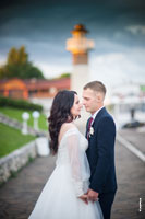 Поясное фото жениха с невестой напротив друг друга, держащихся за руки, на фоне маяка комплекса «Белый берег»