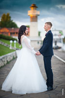 Фото жениха с невестой в полный рост, в профиль, напротив друг друга, на фоне маяка, держащихся за руки и смотрящих друг на друга