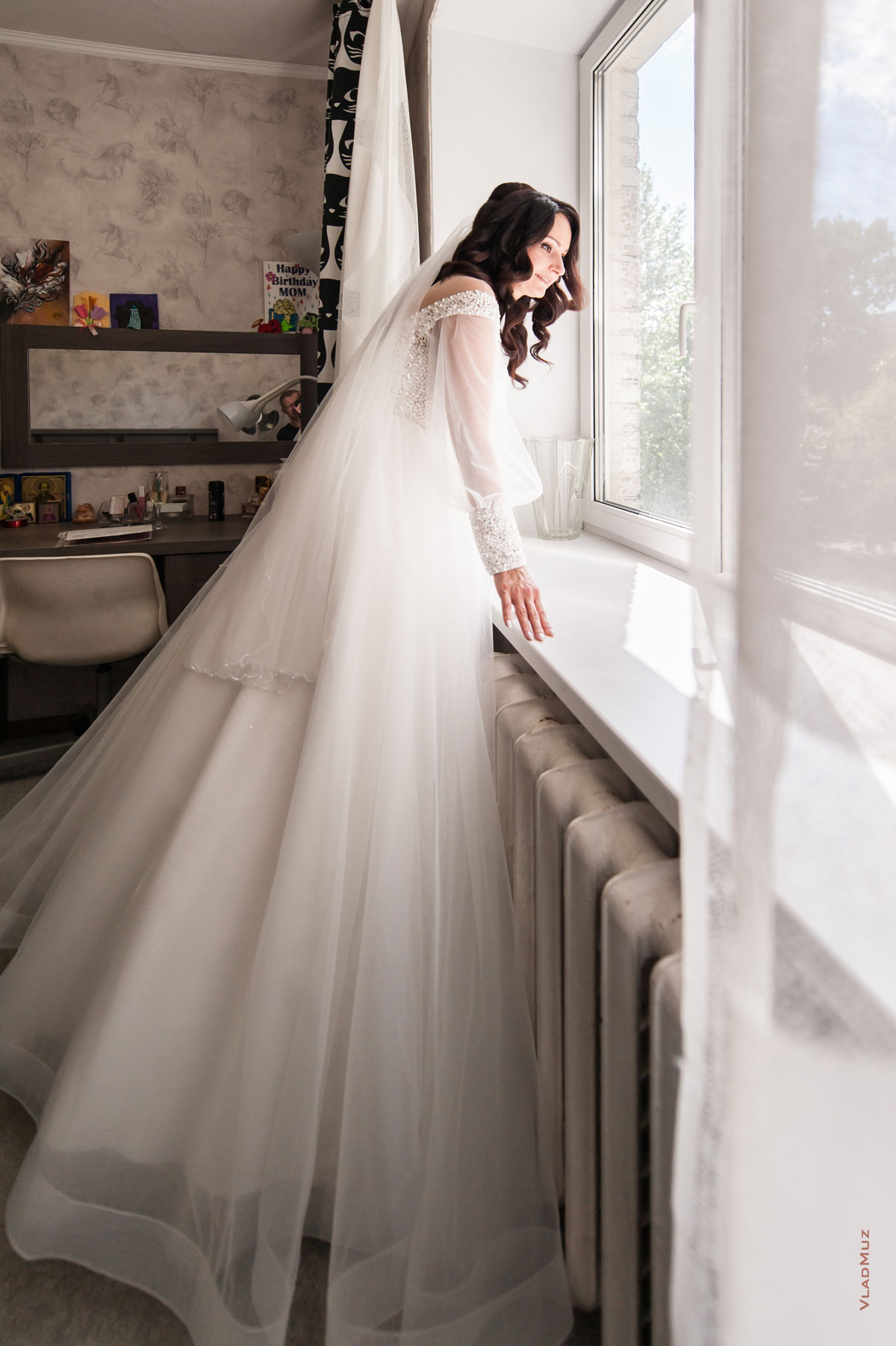 Фото невесты в свадебном платье в полный рост у окна в ожидании жениха