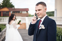 Фото жениха с телефоном в фокусе, вдали стоит невеста — в расфокусе
