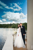 Свадебный фотопортрет молодоженов в полный рост на фоне реки и облачного неба