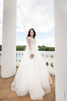 Свадебное фото невесты в светлых тонах: красивая невеста в белом платье в полный рост на фоне облаков и колонн ротонды