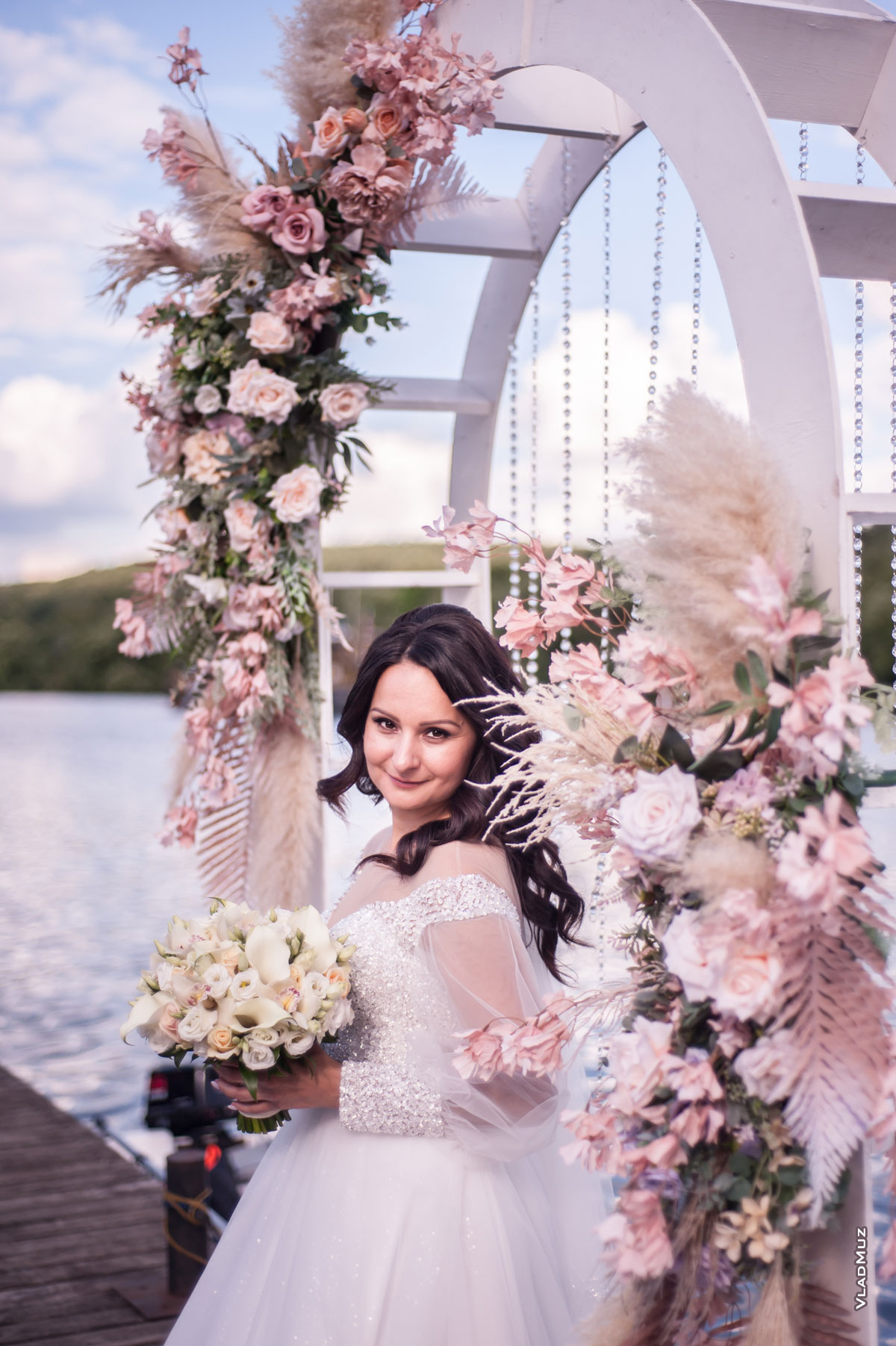 Фото красивой невесты с букетом на фоне свадебной арки