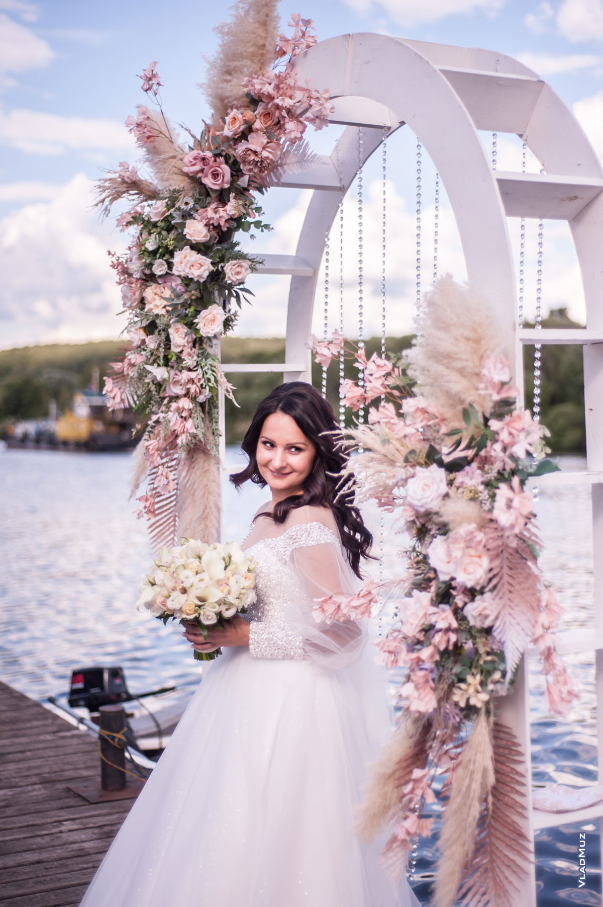 Фото красивой невесты с улыбкой на фоне цветочной свадебной арки