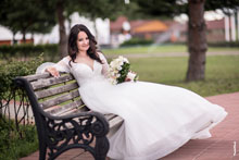 Фото невесты с букетом, сидя на лавочке в свадебном платье, в полный рост