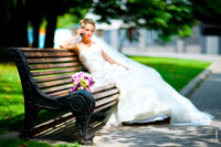 Фото букета невесты на лавочке в фокусе, невеста вдали говорит по телефону — в расфокусе