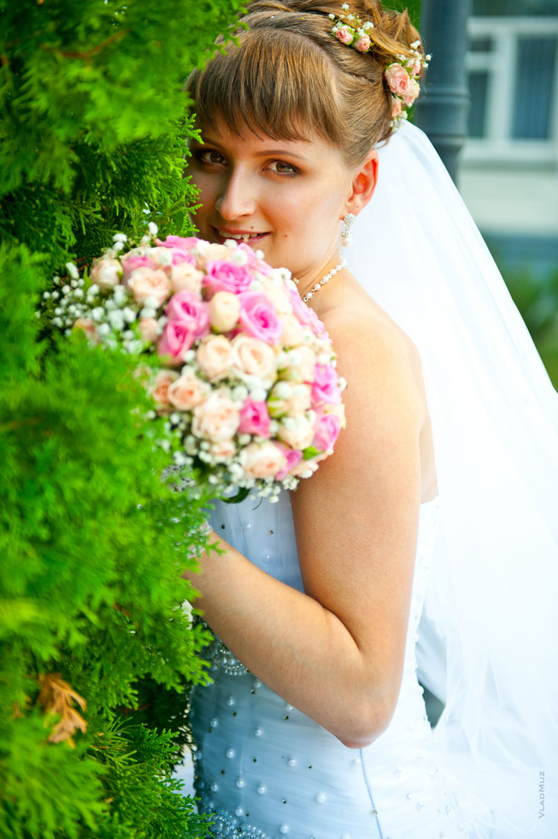 Фотография невесты с букетом среди хвойных ветвей туи