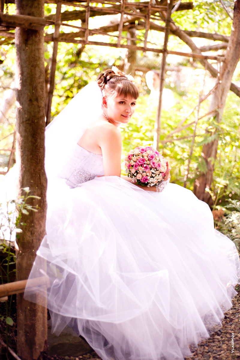 Фото сидящей на лавочке невесты в тенистой аллее ботанического сада Толоконникова