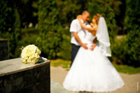 Фото букета невесты на переднем плане в фокусе, свадебной пары вдали в расфокусе