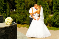 Фото букета невесты на переднем плане в фокусе, поцелуй молодоженов вдали в расфокусе