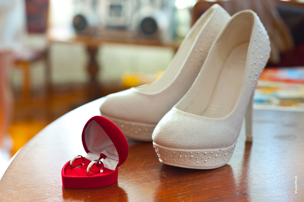 Фото красной коробочки с обручальными кольцами и белых туфель невесты на высоких каблуках