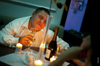Фотопортрет жениха с бокалом шампанского при свете свечей, за столом в кафе