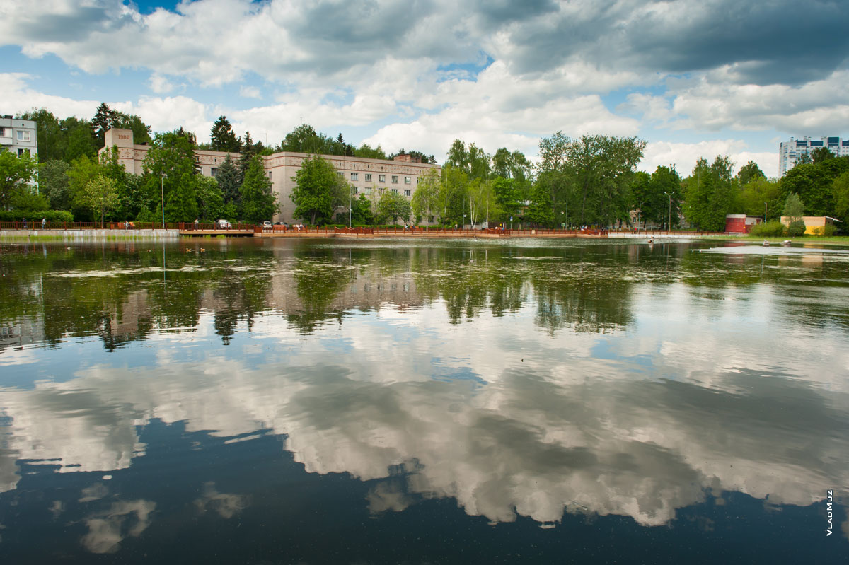 Фото озера и здания гостиницы в мкрн. Юбилейном г. Королёва Московской области на фоне синего облачного неба и его отражения в воде. Летний фотопейзаж