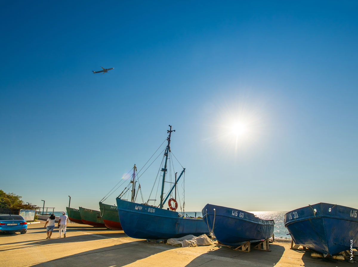 Лодки на набережной Адлера и летящий самолет в небе. Фотопейзаж